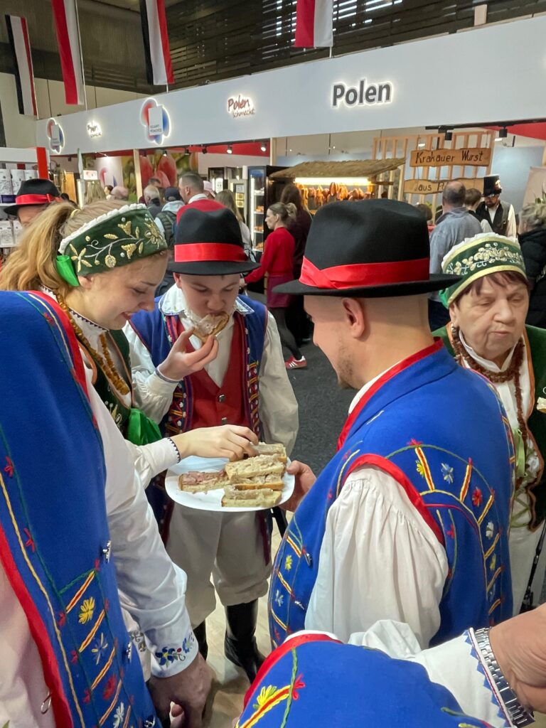 Grupa osób w strojach kaszubskich degustuje chleb ze smalcem