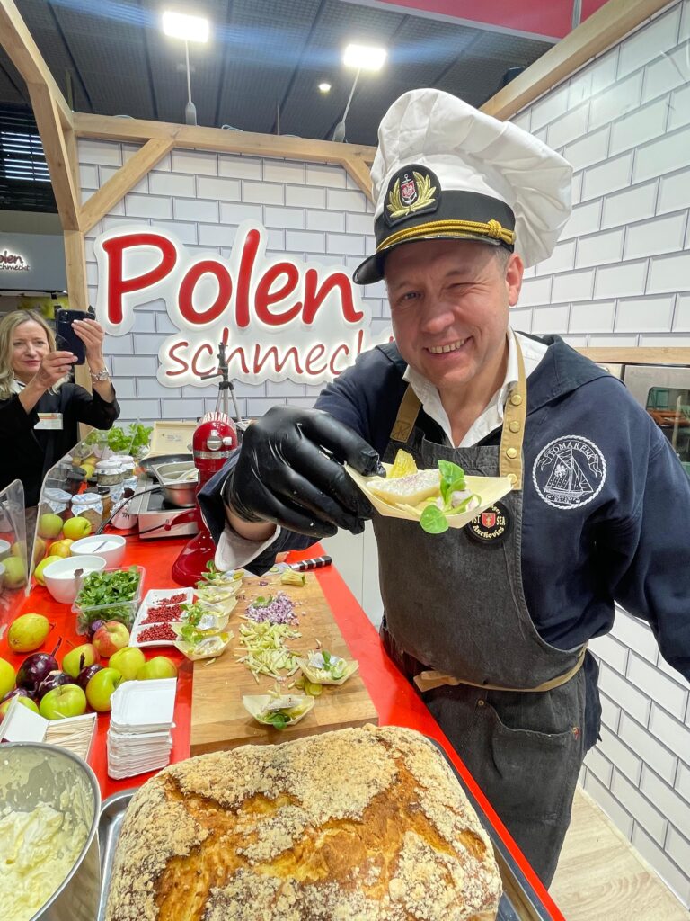 uśmiechnięty kucharz prezentuje degustacyjne danie ze śledziem