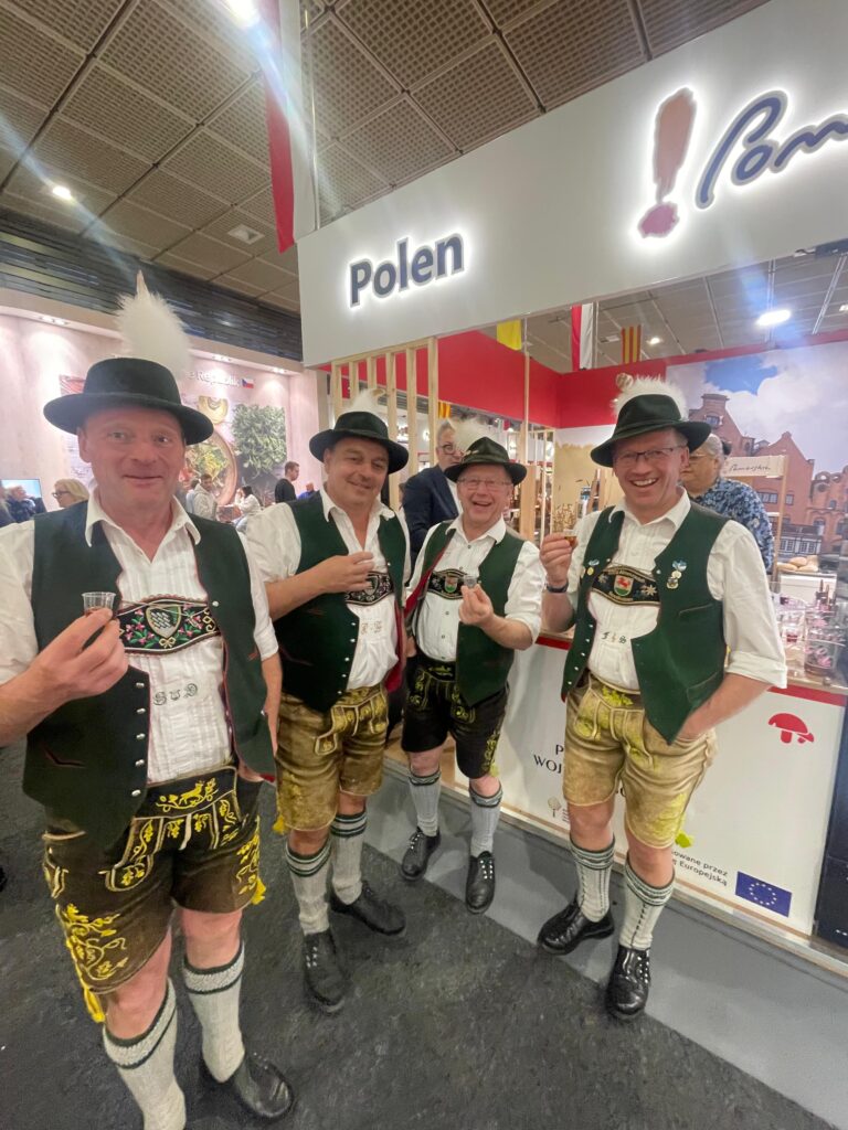 Czterech panów w strojach bawarskich degustuje napój przy stoisku województwa pomorskiego